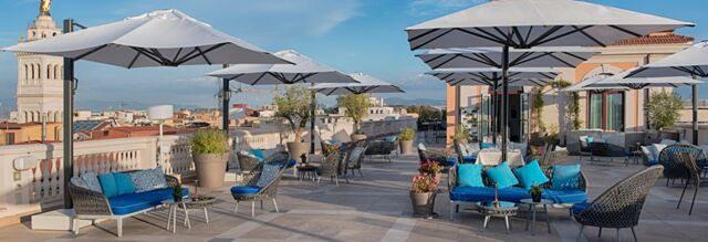 Outdoor terrace seating with umbrellas, blue cushions, potted plants, and city view at NH Collection Roma Palazzo Cinquecento