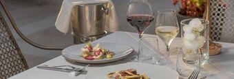 Two plates with gourmet dishes, two glasses of red and white wine, and a flower vase on a white table at NH Collection Roma Palazzo Cinquecento