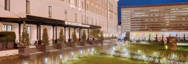 Night view of the outdoor seating area and entrance of NH Collection Roma Palazzo Cinquecento with illuminated garden and modern building background