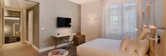 Modern hotel room at NH Collection Roma Palazzo Cinquecento with large bed, desk, chair, wall-mounted TV, and floor mirror