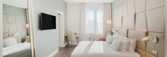 Bright hotel room at NH Collection Roma Palazzo Cinquecento with large bed, wall-mounted TV, desk, and beige padded wall panels