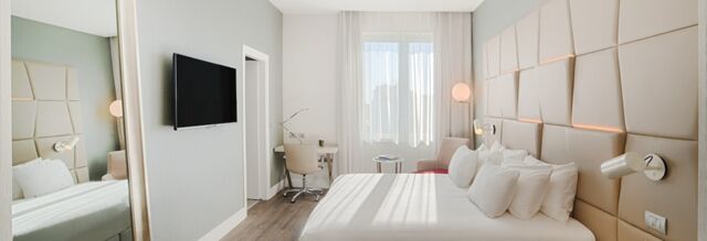 Bright hotel room at NH Collection Roma Palazzo Cinquecento with large bed, wall-mounted TV, desk, and beige padded wall panels