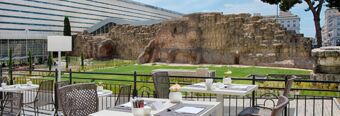 Outdoor dining area with tables and chairs overlooking ancient stone ruins near NH Collection Roma Palazzo Cinquecento