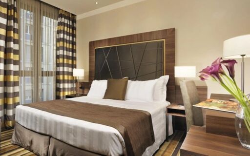 A neatly made bed with white linens and brown accents in a room at Uptown Palace Hotel with bedside lamps and floral decor