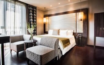 Bright hotel room at Uptown Palace Hotel featuring a king bed with white linens and patterned armchairs by a window