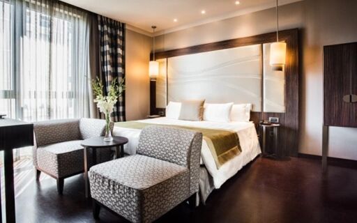 Bright hotel room at Uptown Palace Hotel featuring a king bed with white linens and patterned armchairs by a window