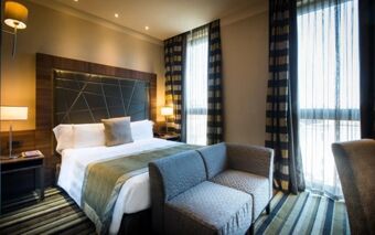 Hotel room at Uptown Palace Hotel featuring a large bed, side tables with lamps, a small couch, and tall windows with striped curtains