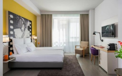Hotel room at NYX Hotel Milan with twin beds, a large black and white artwork, a chair, desk, and TV on the wall