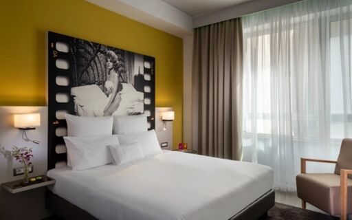 NYX Hotel Milan room with a large bed, white bedding, black and white wall art, two wall lamps, and a sheer curtain window