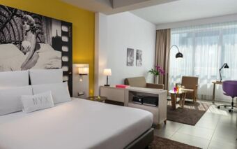 Modern hotel room at NYX Hotel Milan with a large bed, black and white wall art, seating area, and large window curtains