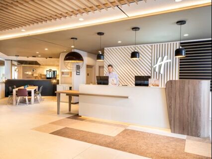 Moderne Empfangstheke mit einem Mitarbeiter im Eingangsbereich des Holiday Inn Mannheim City - Hauptbahnhof, hell und einladend gestaltet.