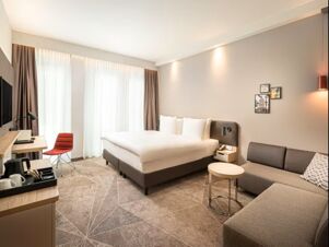 Modern eingerichtetes Hotelzimmer mit Doppelbett, Sofa und Schreibtisch im Holiday Inn Mannheim City - Hauptbahnhof mit gro&szlig;en Fenstern.