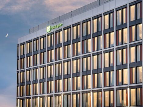 Moderne Fassade des Holiday Inn Mannheim City - Hauptbahnhof mit vielen Fenstern und beleuchteten Zimmern bei D&auml;mmerung unter einem leicht bew&ouml;lkten Himmel.