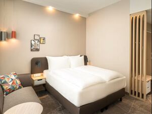 Modern eingerichtetes Hotelzimmer mit Doppelbett, Sofa und dekorativen Bildern im Holiday Inn Mannheim City - Hauptbahnhof.
