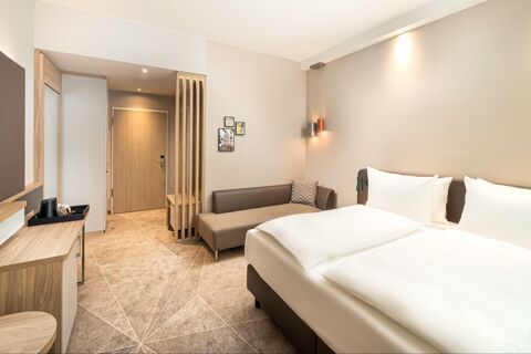 Modern eingerichtetes Hotelzimmer mit gro&szlig;em Bett und Sofa im Holiday Inn Mannheim City - Hauptbahnhof in dezenten Farben und guter Beleuchtung.