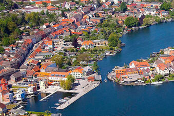 Aerial view of a lakeside town with docks, boats, green trees, and buildings with red roofs near Hotel zur Sonne