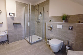Modern bathroom in Hotel zur Sonne with glass shower, wall-mounted toilet, tiled walls, and metal towel rack with towels