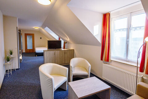 A hotel room at Hotel zur Sonne with two white armchairs around a wooden coffee table, a TV, and a bed near a wooden door