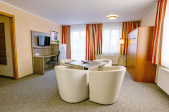 A modern hotel room at Hotel zur Sonne with four white leather chairs around a wooden table and a desk area with TV.