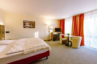 Hotel zur Sonne spacious room with double bed, desk, TV, armchairs, table, red curtains, and swan picture on wall