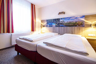 Bright hotel room at Hotel zur Sonne with two single beds, a large window with striped curtains, and boat-themed artwork above the headboard