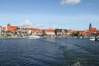 A large body of water with boats docked near the shore and a row of buildings with orange roofs including Hotel zur Sonne in the background