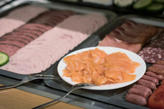 A plate with slices of smoked salmon placed on a buffet table with various cold cuts at Hotel zur Sonne