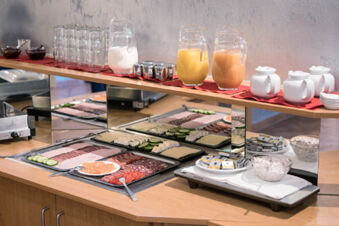 Cold cuts, sliced cheese, condiments, glasses, pitchers of juice, and white jars arranged for breakfast at Hotel zur Sonne