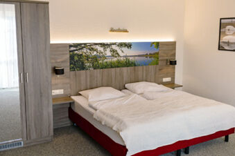 Hotel zur Sonne room with double bed, wooden headboard with landscape photo, two pillows, wardrobe, and wall lamps