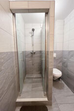 Helle Dusche mit Glasw&auml;nden und modernem Duschkopf neben einer Toilette im Badezimmer des G&auml;stehaus Odin mit grauen und wei&szlig;en Fliesen.