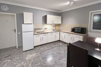 Moderne und funktionale Gemeinschaftsk&uuml;che mit wei&szlig;en Schr&auml;nken, K&uuml;hlschrank, Mikrowelle und Essbereich im G&auml;stehaus Odin.