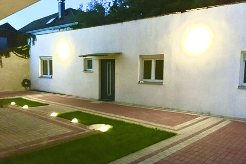 Die beleuchtete Fassade des G&auml;stehaus Odin zeigt einen modernen Eingang mit zwei Fenstern und einem gepflasterten Weg bei D&auml;mmerung.