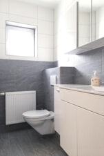 Modernes Badezimmer mit Wand-WC, Waschbecken und fliesen in Grau-Wei&szlig; bei G&auml;stehaus Odin mit nat&uuml;rlichem Licht durch Fenster.