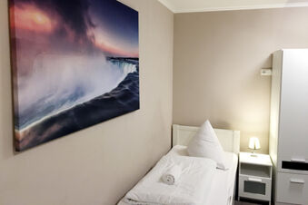 Schlicht eingerichtetes Einzelzimmer mit wei&szlig;er Bettw&auml;sche und Nachttischlampe im G&auml;stehaus Odin, dekoriert mit einem Wasserfall-Bild.