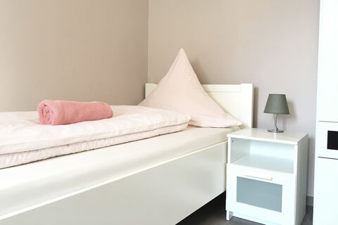 Schlicht eingerichtetes Einzelzimmer mit wei&szlig;em Bett, rosa Handtuch und Lampentisch im G&auml;stehaus Odin mit gem&uuml;tlichem Ambiente.
