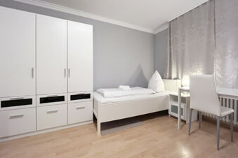 Schlicht eingerichtetes Einzelzimmer mit Kleiderschrank, Bett und Schreibtisch im G&auml;stehaus Odin mit hellem Holzboden.