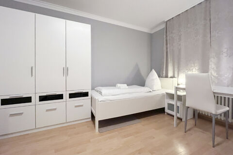 Schlicht eingerichtetes Einzelzimmer mit Kleiderschrank, Bett und Schreibtisch im G&auml;stehaus Odin mit hellem Holzboden.