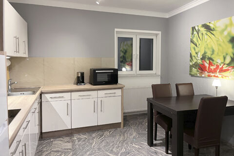 Moderne K&uuml;che mit wei&szlig;en Schr&auml;nken, Mikrowelle, Kaffeemaschine und Essbereich im G&auml;stehaus Odin mit dekorativem Wandbild.