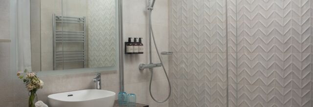 Modern bathroom with white sink, mirror, shower area with glass partition, and toiletries at Hotel NH Collection Roma Fori Imperiali