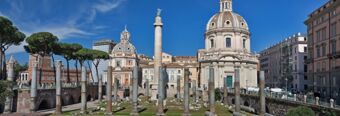 Ancient Roman ruins with columns and the Trajan&rsquo;s Column surrounded by historic buildings under clear blue sky near Hotel NH Collection Roma Fori Imperiali