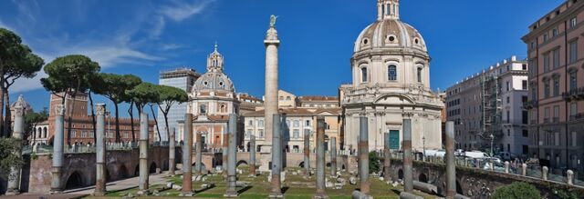 Ancient Roman ruins with columns and the Trajan&rsquo;s Column surrounded by historic buildings under clear blue sky near Hotel NH Collection Roma Fori Imperiali