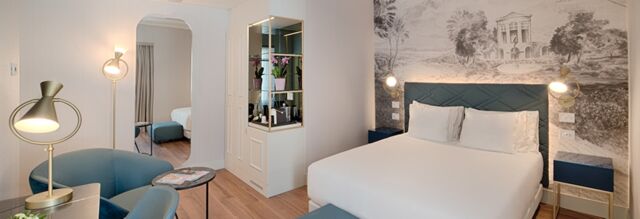 Bright hotel room at Hotel NH Collection Roma Fori Imperiali with white bed, blue armchair, wooden floor, and black and white wall art