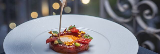 A gourmet dish with sauce being poured over an egg yolk surrounded by garnishes on a white plate at Hotel NH Collection Roma Fori Imperiali