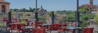 Outdoor dining area with red chairs and glass-railed terrace with city views at Hotel NH Collection Roma Fori Imperiali