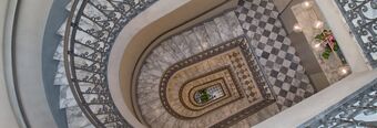 Spiral marble staircase with ornate iron railings and checkered tile floor at Hotel NH Collection Roma Fori Imperiali