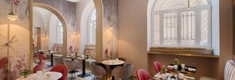 Dining area at Hotel NH Collection Roma Fori Imperiali with marble tables, red and gray chairs, and arched windows with iron grilles