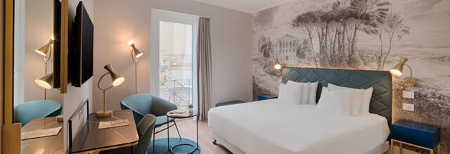 Hotel NH Collection Roma Fori Imperiali room with king bed, two blue chairs, desk with lamp, wall mural, and window view