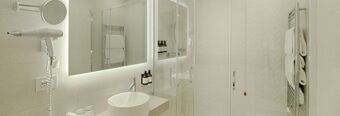 Bathroom with illuminated mirror, wall-mounted hairdryer, shower area, and towel racks in Hotel NH Collection Roma Fori Imperiali