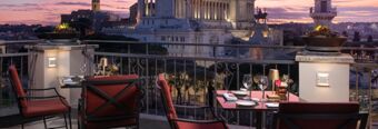 Outdoor terrace seating with red cushioned chairs and tables set for dining at Hotel NH Collection Roma Fori Imperiali at sunset