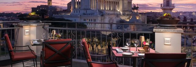 Outdoor terrace seating with red cushioned chairs and tables set for dining at Hotel NH Collection Roma Fori Imperiali at sunset
